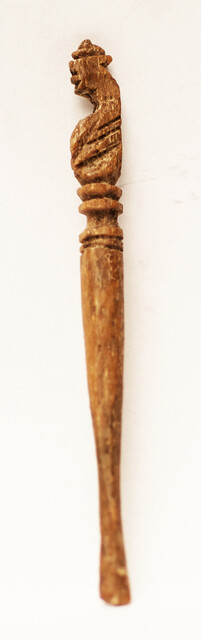 A seventeenth century bone ear-spoon crowned by a man with a hat.